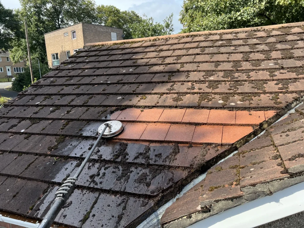 Red roof tiles being cleaned of moss by a surface pressure washer